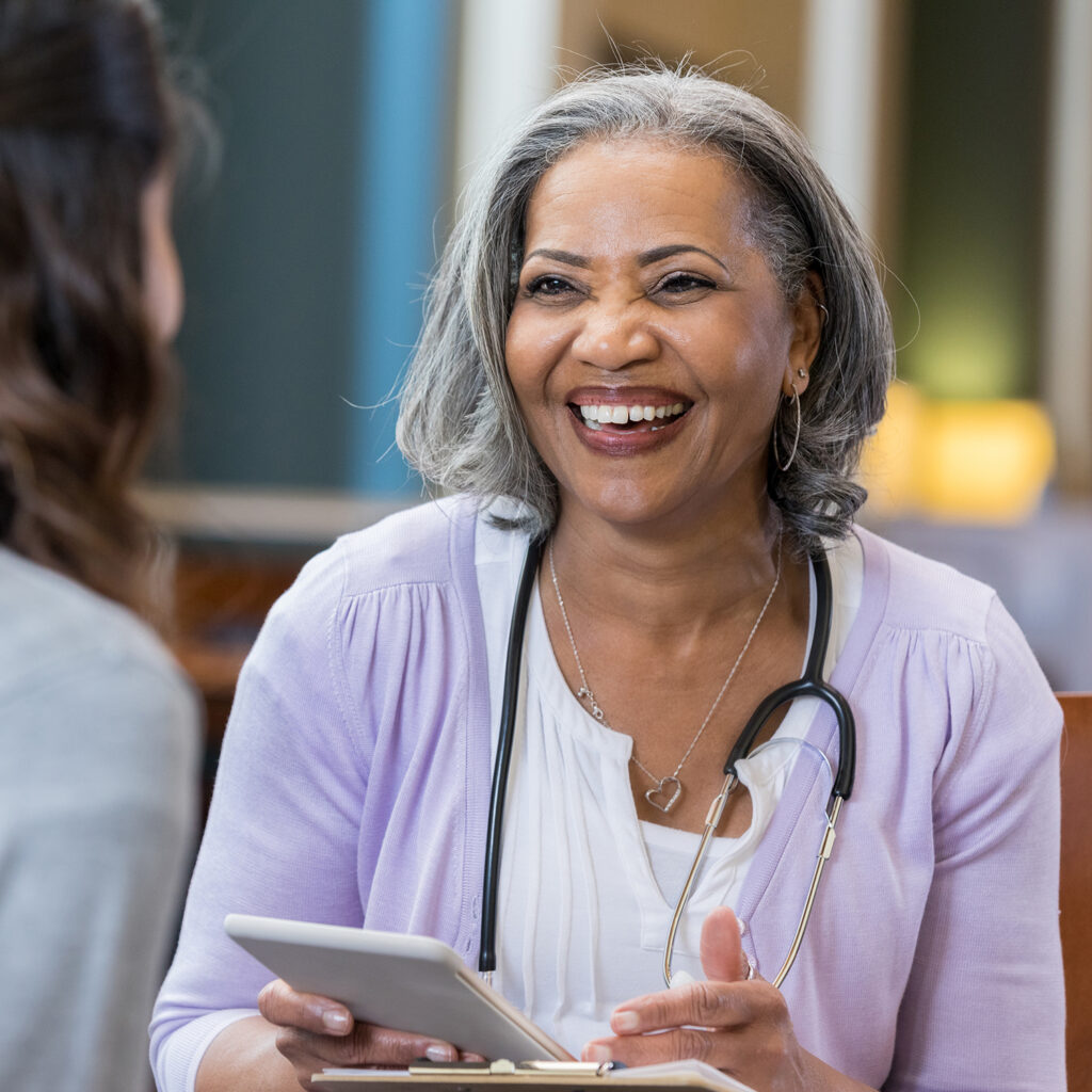 Confident African American female medical school professor talks with female student. The professor is holding a digital tablet.